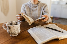 a woman sitting down at a table with a Bible, journal, and coffee mug 