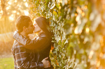 Man and woman leaning against ivy covered wall kissing.