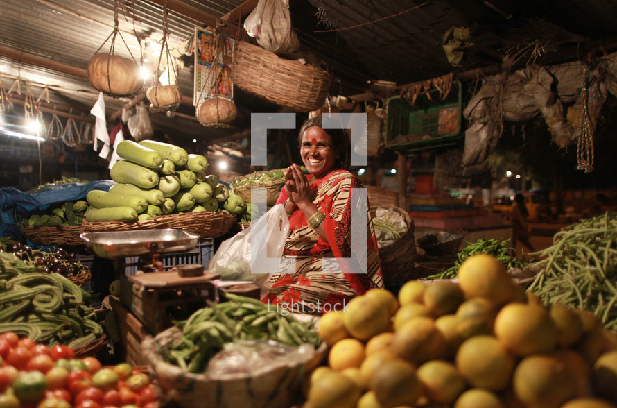 woman in India sitting with her hands together in a vegetable market