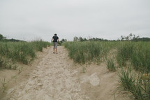 a young man walking on a sandy path on a beach 