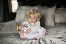 big sister holding baby sister on a bed 