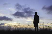 silhouette of a man standing in a field at sunset 