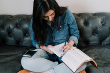 a woman sitting on a couch reading a Bible and taking notes in a journal 