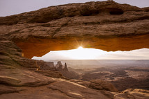 sunlight through a red rock arch over a canyon