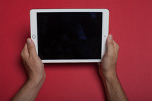 Hands holding an electronic tablet on a red background.