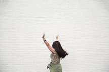 a woman with open arms standing in front of a white wall 