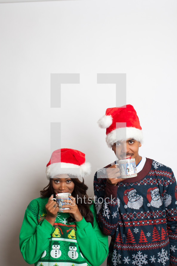 couple in ugly Christmas sweaters and santa hats sipping hot cocoa 