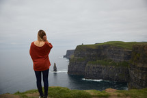 a woman standing at the edge of a cliff taking in the view of the ocean below 