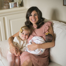 mother holding a swaddled newborn baby and toddler daughter 