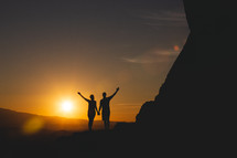silhouette of a couple standing at the edge of a mountain at sunset 