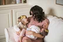 mother holding a swaddled newborn baby and toddler daughter in a chair 