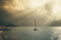 rays of sunlight shining through clouds onto a sailboat 
