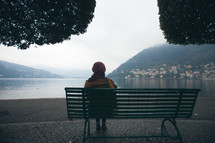 woman sitting on a park bench looking out over a waterway 