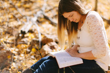 a woman sitting in fall leaves reading a Bible 