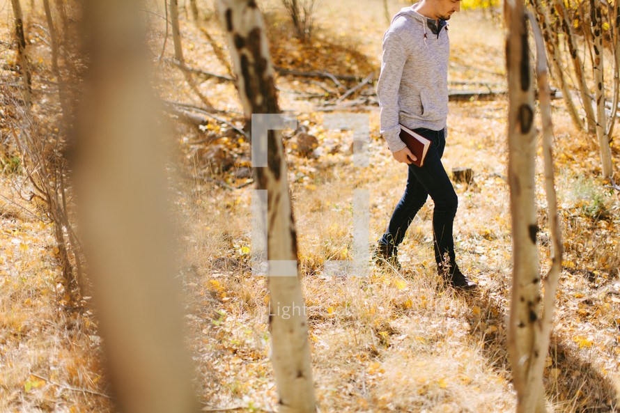 a man walking through a forest carrying a Bible 