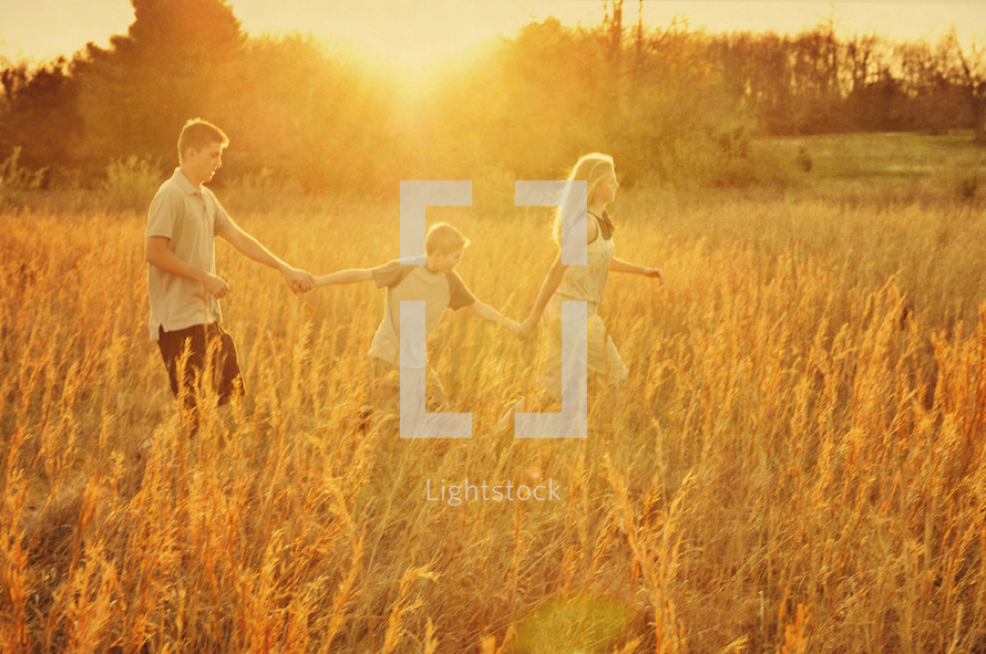 siblings holding hands walking in a field