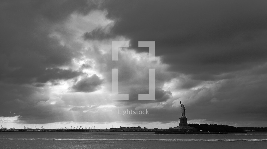 sun shining through the clouds over the Statue of Liberty
