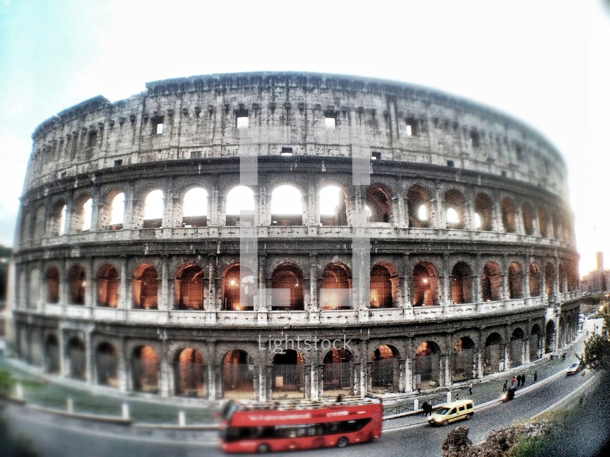 The Colosseum during the day surrounded by red bus and cars in traffic.