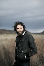 man with a beard standing alone in a field 