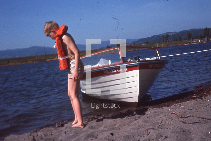 child on a shore in front of a boat 