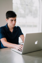 a teen boy typing on a laptop computer 