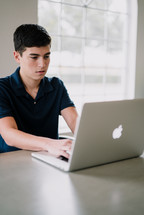 a teen boy sitting in front of a laptop computer 