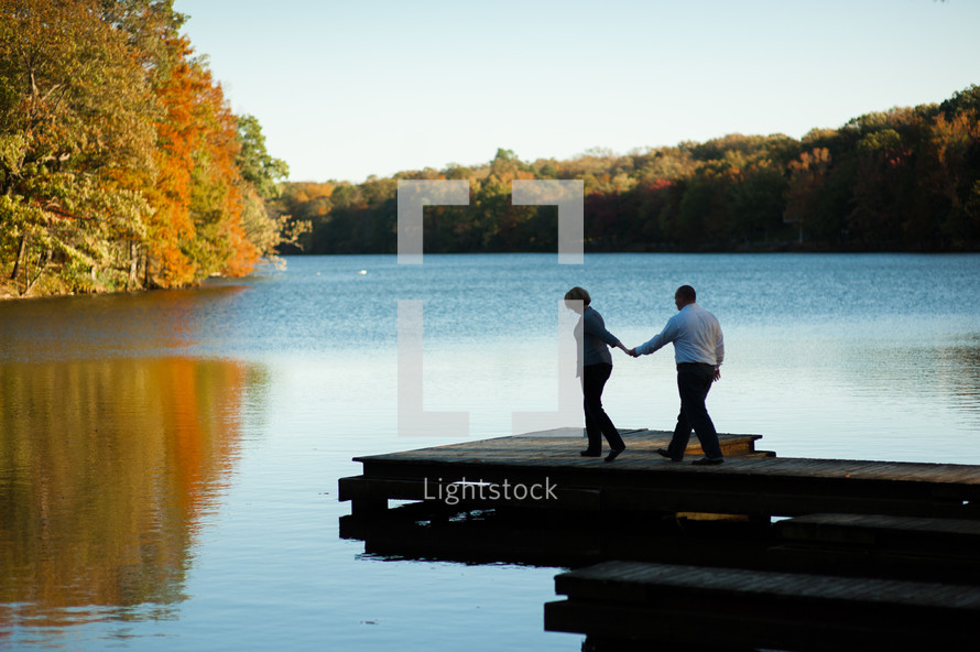 Couple walking on dock together with the fall colors over a lake.
