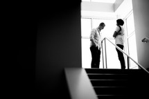 man and woman standing at the top of stairs talking 
