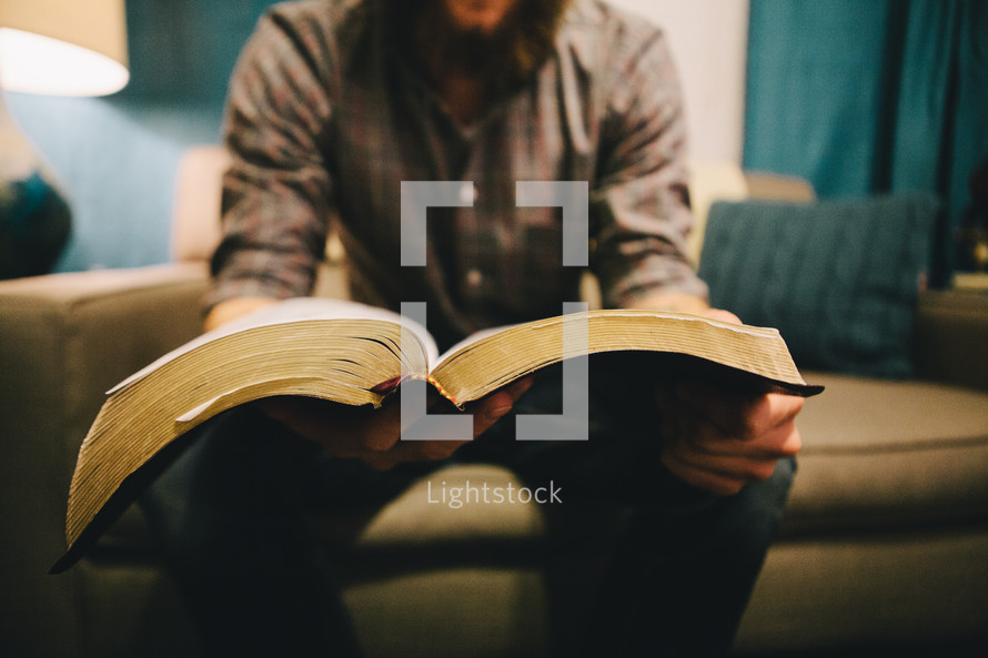 A man sitting on a couch reading a Bible. 