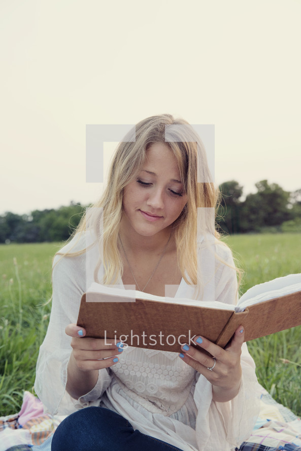 woman sitting in the grass reading a journal.