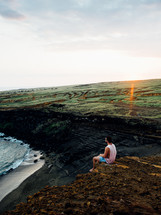 man sitting on a cliff along the shores of Hawaii 
