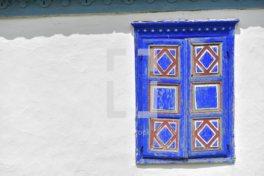 Closed vintage blue and red window on white wall of old traditional house in romania