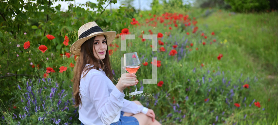 Young woman with Rose Wine In Glass on poppy field