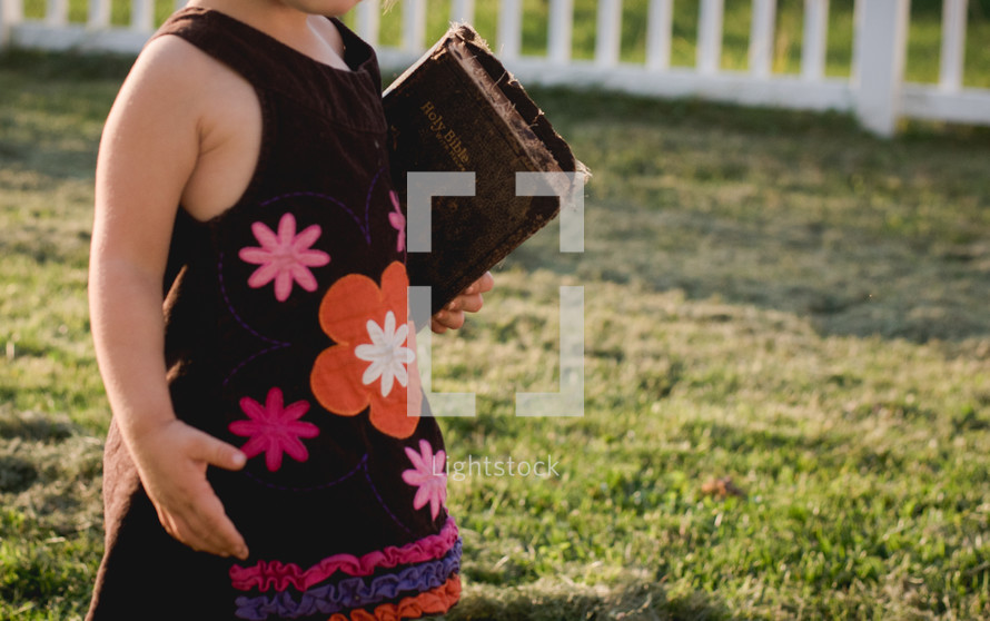toddler girl in a dress carrying a Bible 
