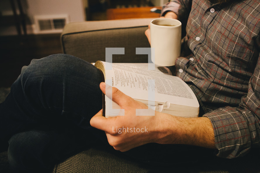 A man sitting on his couch reading a Bible. 