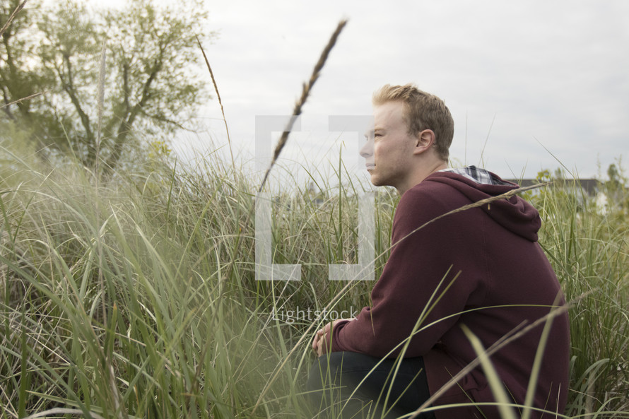 a man sitting in tall grass and praying quietly