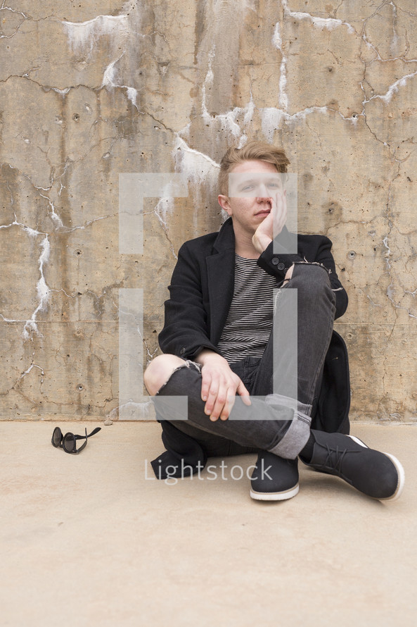 a bored young man sitting on a sidewalk 