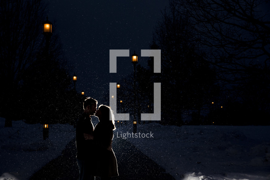 Silhouette of a couple kissing in the snowfall at night.