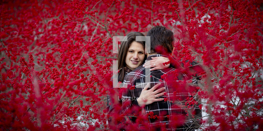 a couple hugging between branches covered with red berries