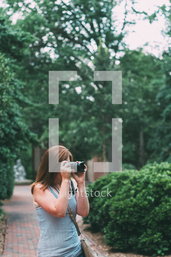 woman standing on a cobblestone sidewalk taking pictures with her camera 