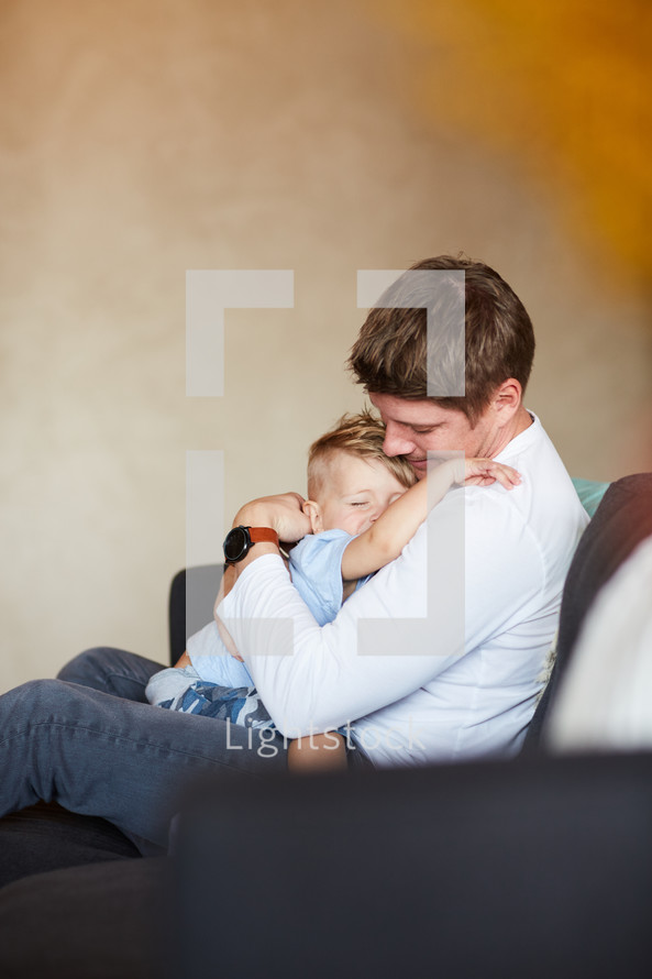 a father holding his son on a couch 