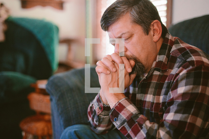 a man sitting on a couch praying 