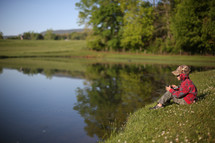 a child sitting at the edge of a pond fishing 