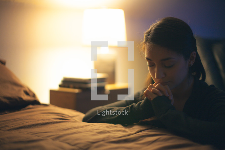 A young woman kneeling by her bed and praying