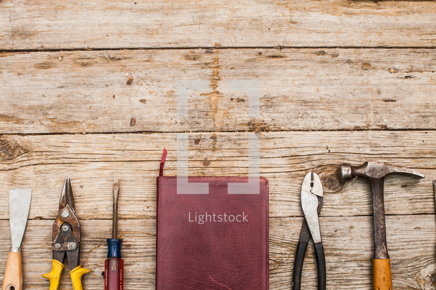 Tools and a Bible lined up on a rustic wooden table.
