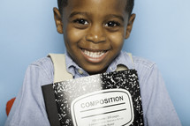 a smiling boy child holding a composition notebook 