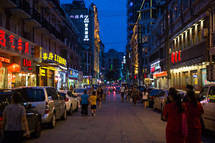 pedestrians and parked cars on a street at night in China 