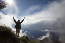 a man standing on a mountain with raised hands 