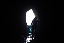 Silhouette of a person walking through a cave entrance toward the light.