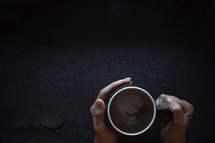 hands holding a coffee mug on dark wooden table.
